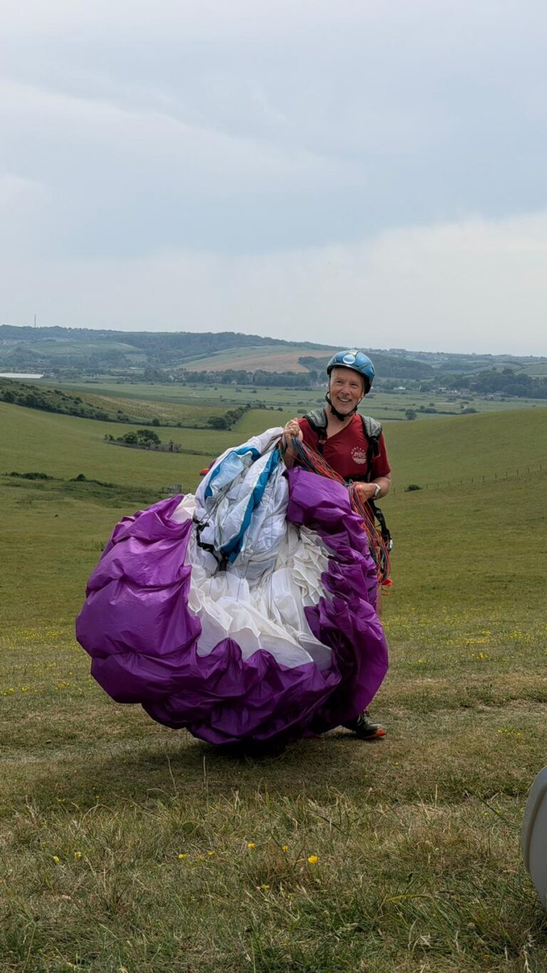 David holding a purple paraglider on a hillside in the South Downs after a beginner paragliding session.