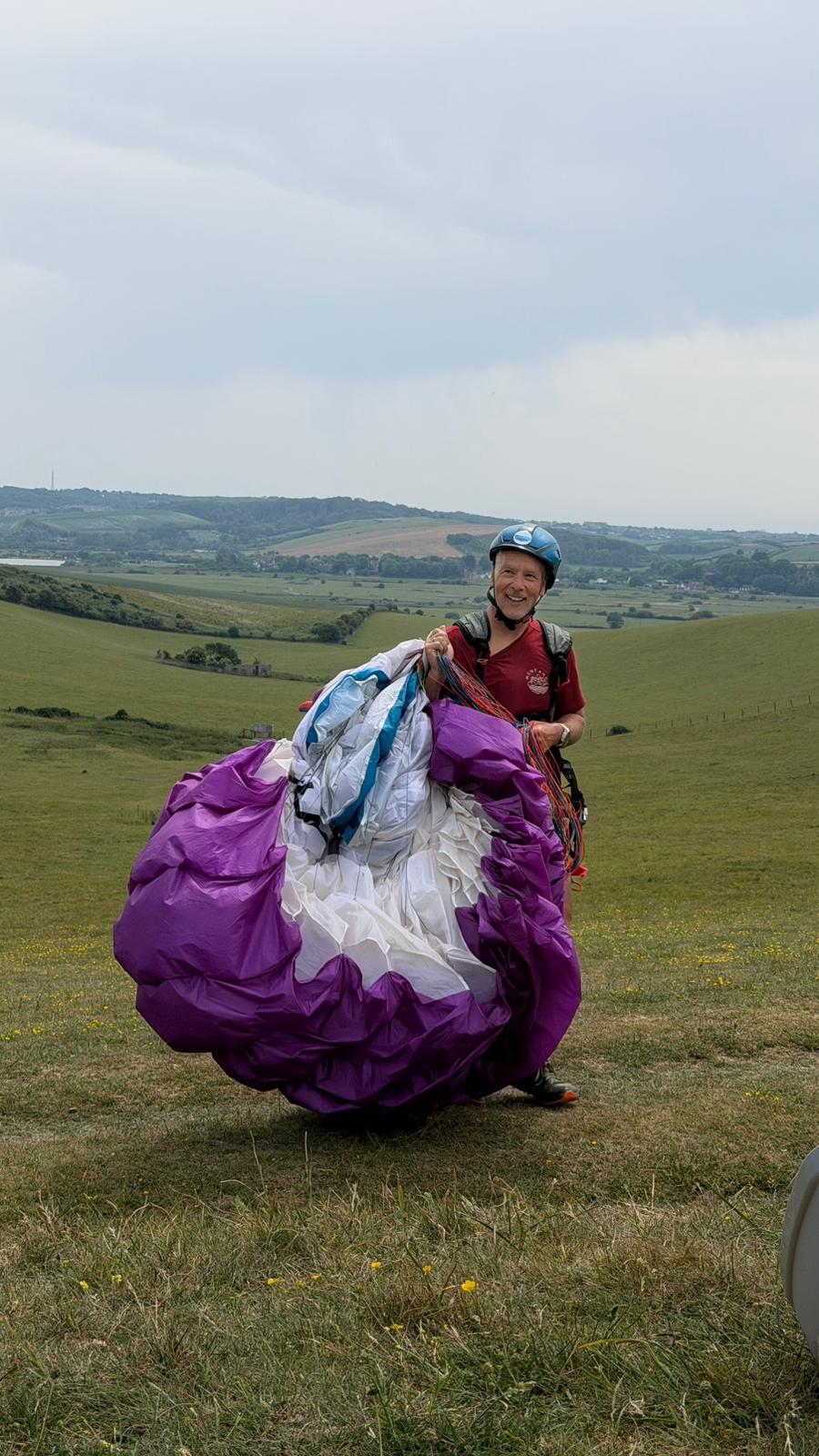 David holding a purple paraglider on a hillside in the South Downs after a beginner paragliding session.